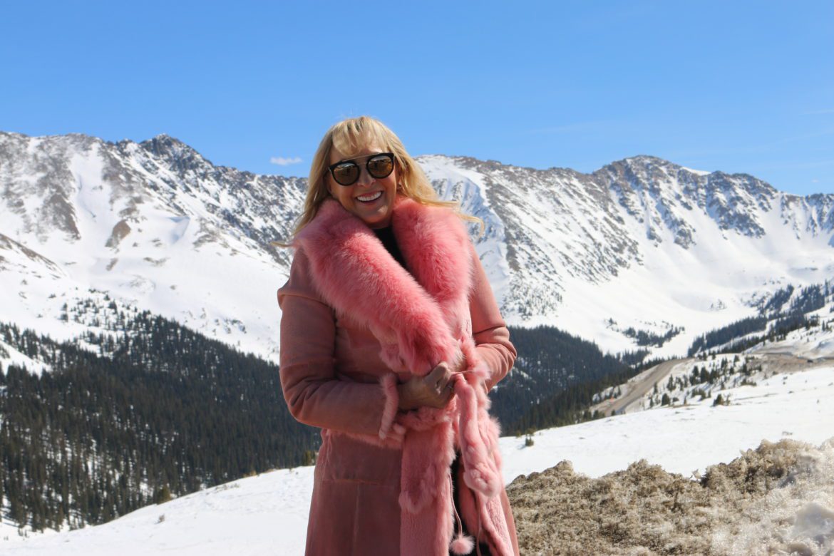 A woman in pink fur coat standing on top of a mountain.