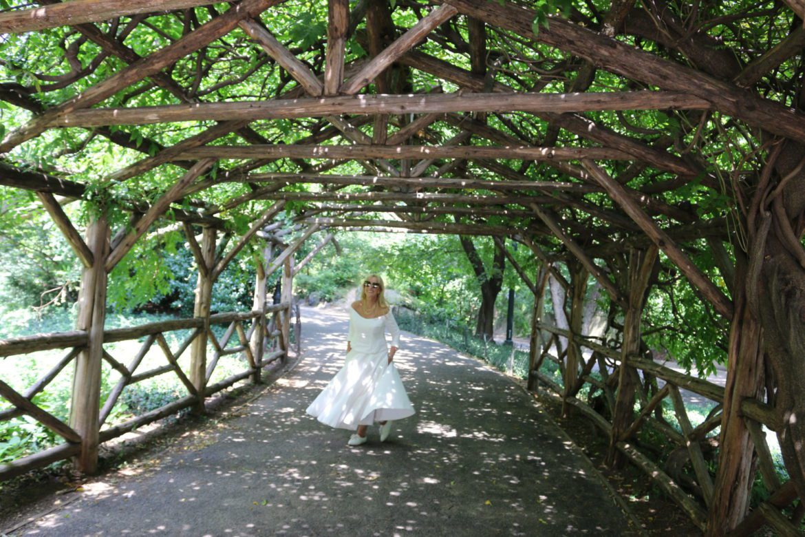 A woman in white dress standing under a wooden structure.