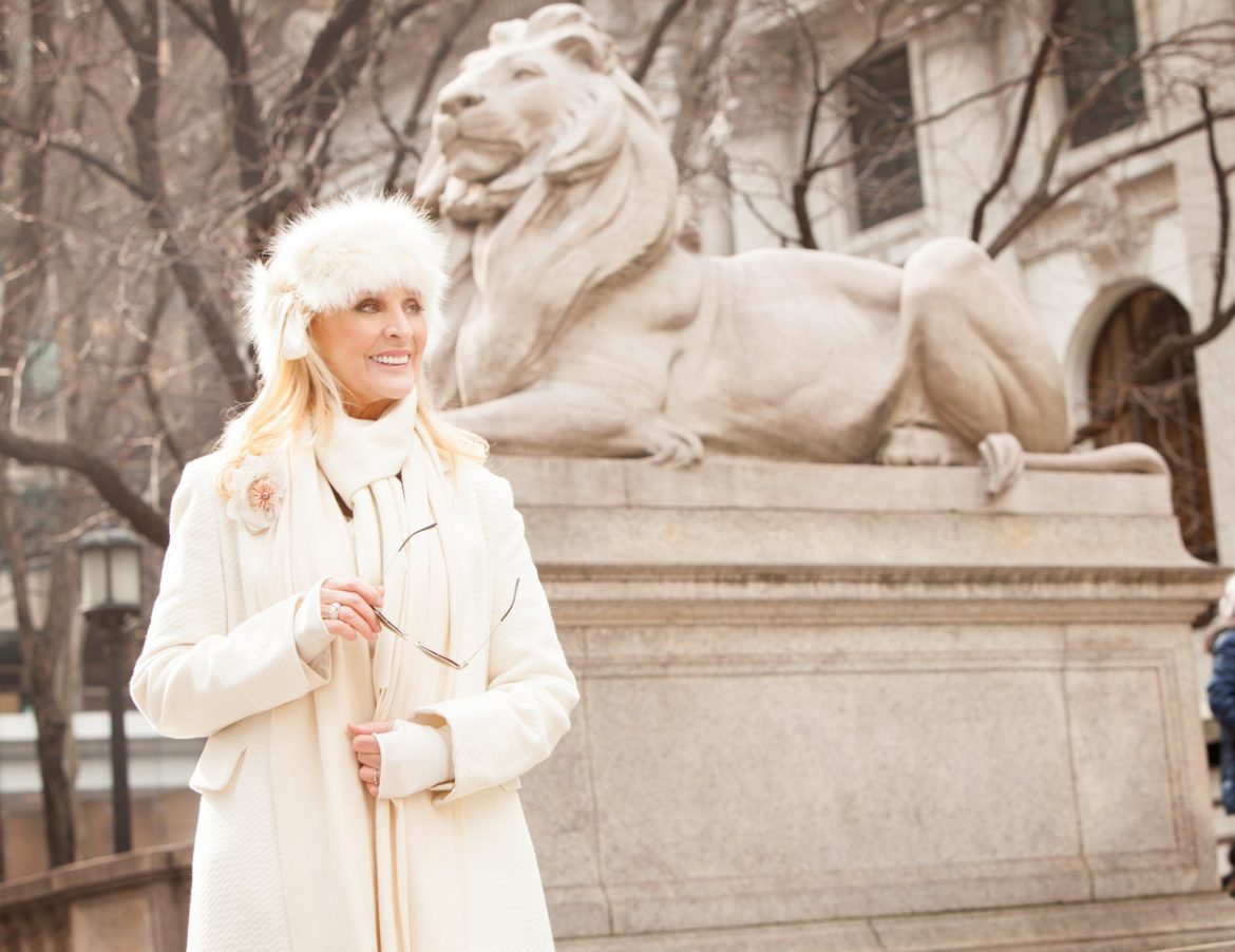 A woman in white coat standing next to lion statue.