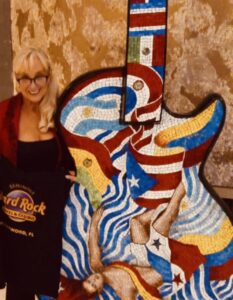Woman posing with a colorful, abstract guitar sculpture indoors.